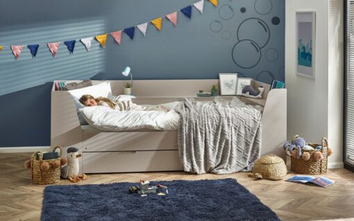 The Cyclone Day Bed in Taupe from Pay Weekly Carpets, dressed with white sheet, duvet and pillow, and a plush pale grey blanket with a chevron pattern, pictured against a blue wall with cotton bunting in the top left corner.